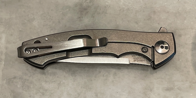 May include: A silver pocket knife with a black handle and a clip. The knife has a partially open blade and the text "GSO  EAF" is visible on the blade.