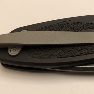 May include: A black pocket knife with a textured handle and a silver pocket clip.