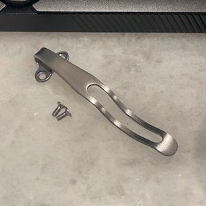 May include: A silver pocket clip for a knife with two screws.