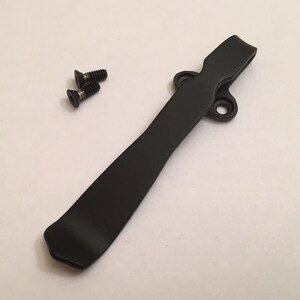 May include: Black metal pocket clip with two small black screws. The clip is designed to attach to a pocket or belt.