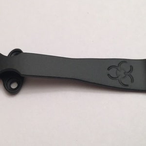 May include: Black metal pocket clip with a biohazard symbol engraved on it.