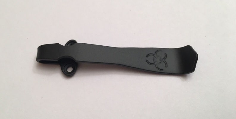 May include: Black metal pocket clip with a biohazard symbol engraved on it.