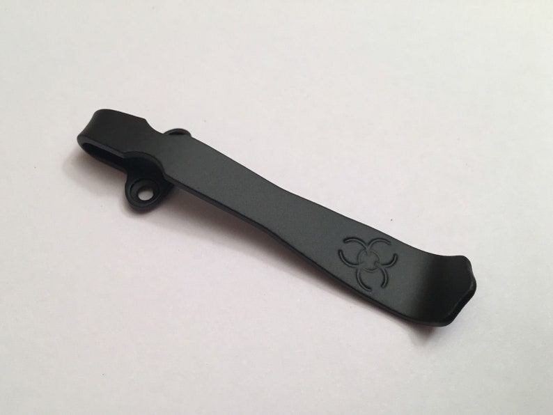 May include: Black metal pocket clip with a biohazard symbol engraved on it.