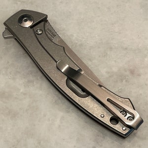 May include: A silver pocket knife with a clip and a D460-141 inscription. The knife is closed and has a textured finish.