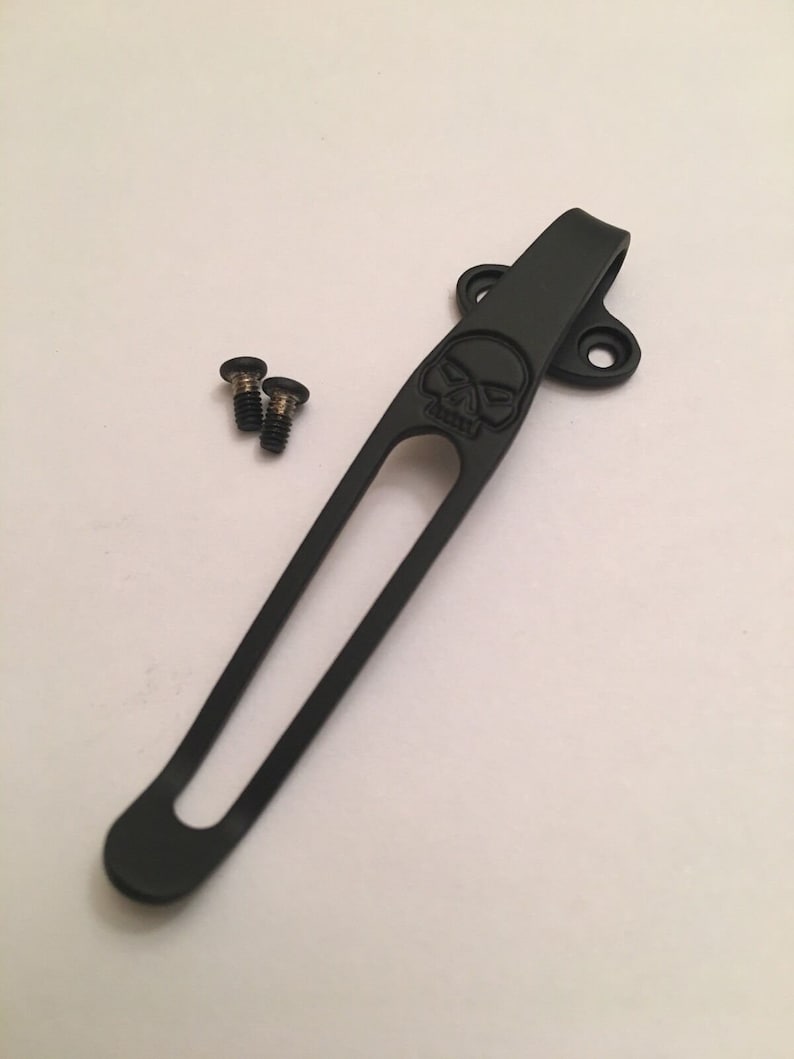 Puede incluir: Clip de bolsillo de metal negro con un dise&ntilde;o de calavera y dos tornillos.