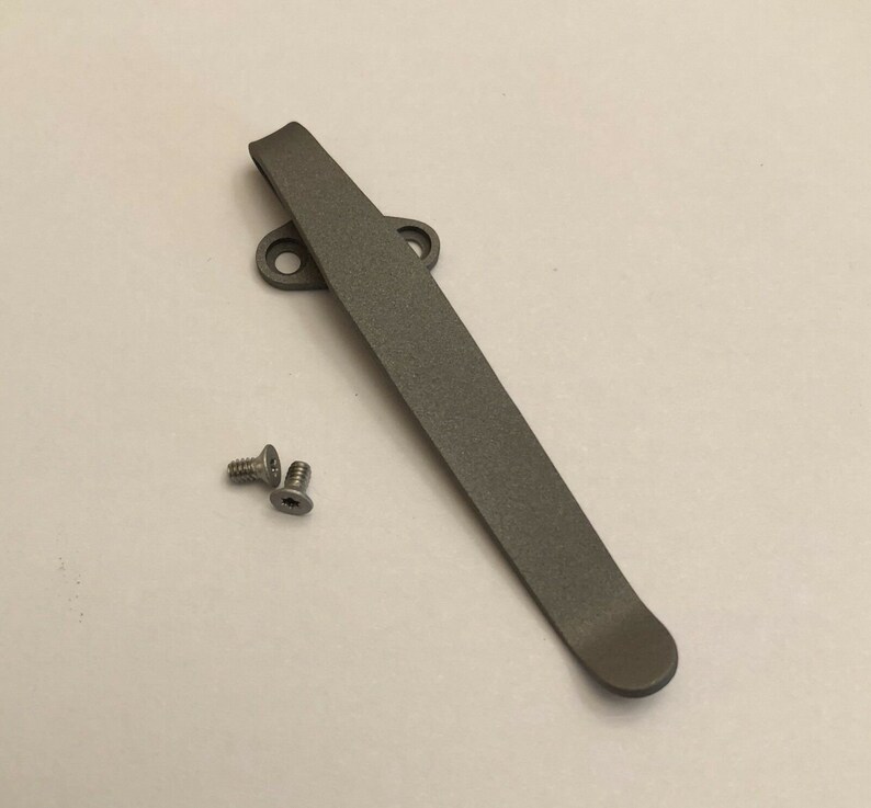 May include: A gray titanium pocket clip with two screws. The clip is designed to attach to a pocket knife or other tool.