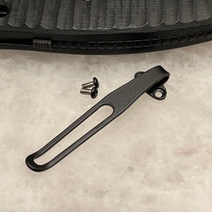 Puede incluir: Clip de bolsillo de metal negro con dos pequeños tornillos negros. El clip está diseñado para sujetarse a una navaja de bolsillo u otra herramienta.