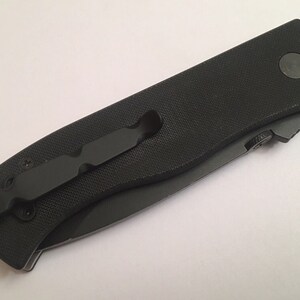 May include: A black pocket knife with a black handle and a pocket clip. The knife has a black blade and a black button on the handle.