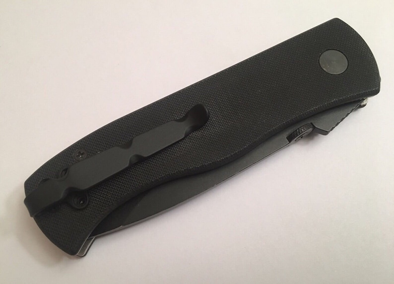 May include: A black pocket knife with a black handle and a pocket clip. The knife has a black blade and a black button on the handle.