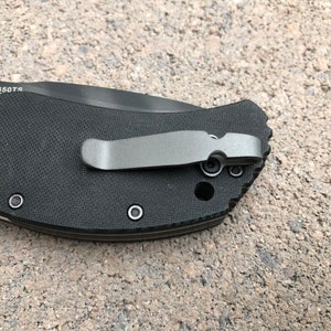 May include: Close-up of a black pocket knife with a silver clip and the text "0350TS" on the handle.