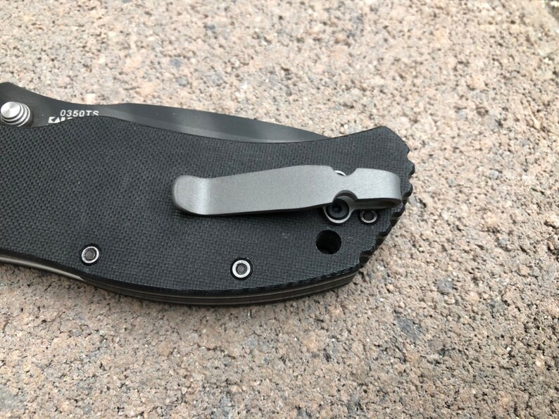 May include: Close-up of a black pocket knife with a silver clip and the text "0350TS" on the handle.