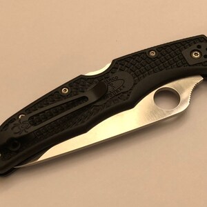 May include: A black pocket knife with a textured handle and a silver blade. The knife has a pocket clip and a Spyderco hole.
