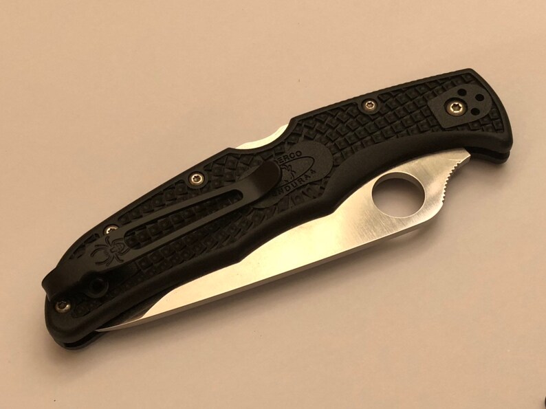 May include: A black pocket knife with a textured handle and a silver blade. The knife has a pocket clip and a Spyderco hole.
