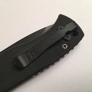 May include: Black pocket knife with a clip and a textured handle. The clip has a logo of three overlapping circles.