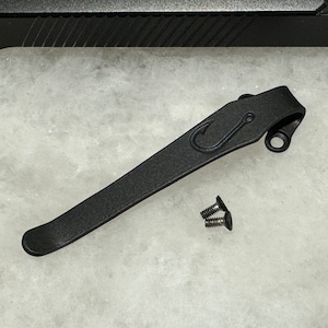 Puede incluir: Clip de bolsillo de metal negro con un diseño de anzuelo de pesca y dos tornillos.