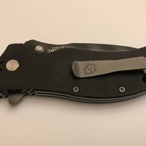 Puede incluir: Un cuchillo plegable negro con mango negro y clip de bolsillo plateado. El cuchillo tiene un mango texturizado y un clip plateado con un logotipo. El cuchillo tiene el n&uacute;mero 0350TS en el lateral.