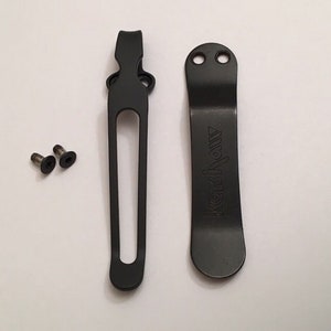 May include: Two black metal pocket clips with a deep black finish. The clip on the right has the word "Kershaw" engraved on it. Two small silver screws are included.