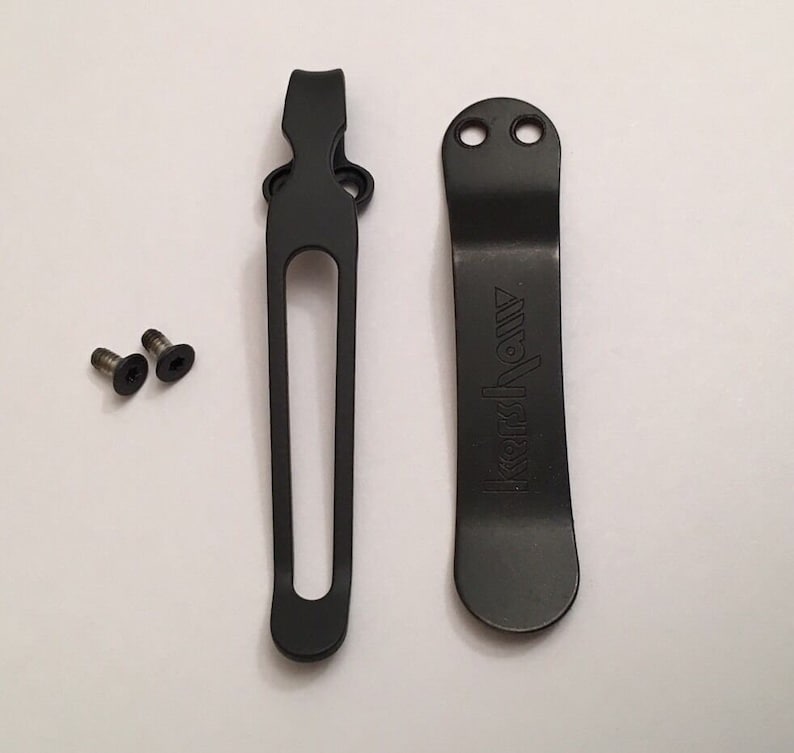 May include: Two black metal pocket clips with a deep black finish. The clip on the right has the word "Kershaw" engraved on it. Two small silver screws are included.
