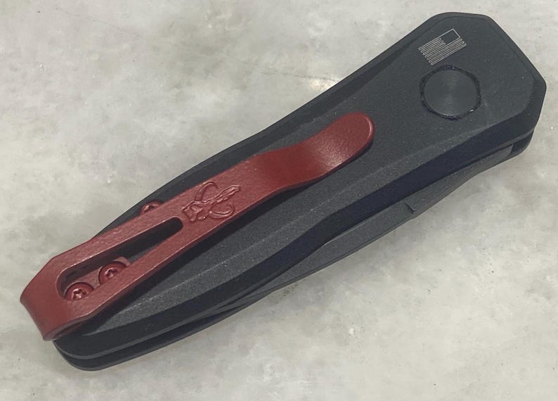 May include: A black pocket knife with a red pocket clip. The knife has a small American flag design on the handle.