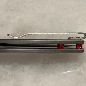 May include: A close-up of a silver pocket knife with a clip and two red accents.