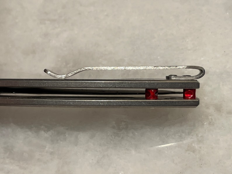May include: A close-up of a silver pocket knife with a clip and two red accents.