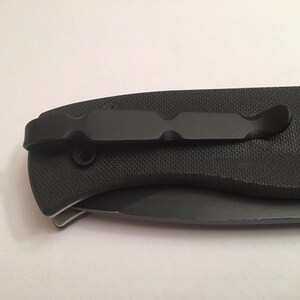 May include: Black pocket knife with a textured handle and a black clip. The knife is closed.