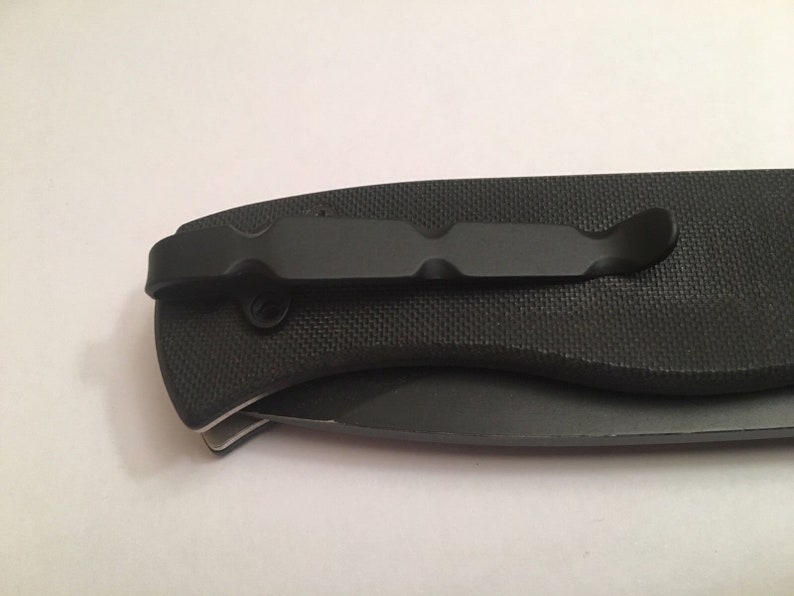 May include: Black pocket knife with a textured handle and a black clip. The knife is closed.