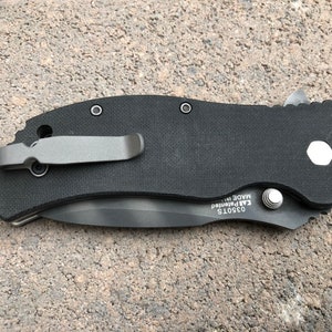 May include: Black pocket knife with a black handle and a silver clip. The knife has a silver screw and the text "03501S  KAI Patented  MADE IN" on the handle.