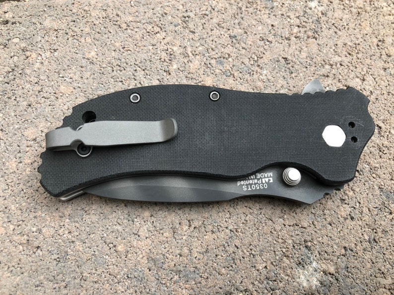 May include: Black pocket knife with a black handle and a silver clip. The knife has a silver screw and the text "03501S  KAI Patented  MADE IN" on the handle.