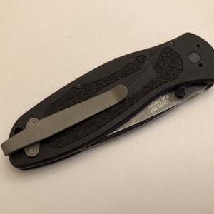 May include: A black folding knife with a textured handle and a pocket clip. The blade is partially open and the knife has the text "MISTRSTM" and "R2" printed on the side.