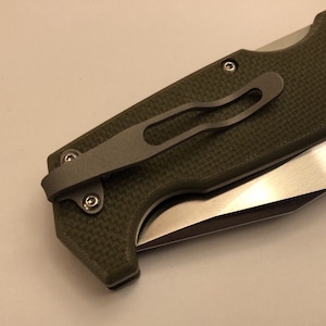 May include: A green pocket knife with a titanium pocket clip. The knife has a partially open blade.