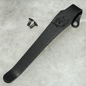May include: A black metal key chain with a textured finish and a small, engraved bulldog head design. The key chain has a hole for attaching keys.