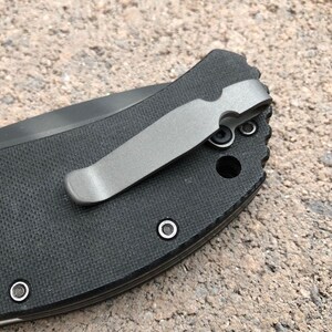 May include: A black pocket knife with a silver pocket clip. The knife has a textured black handle and a silver pocket clip.