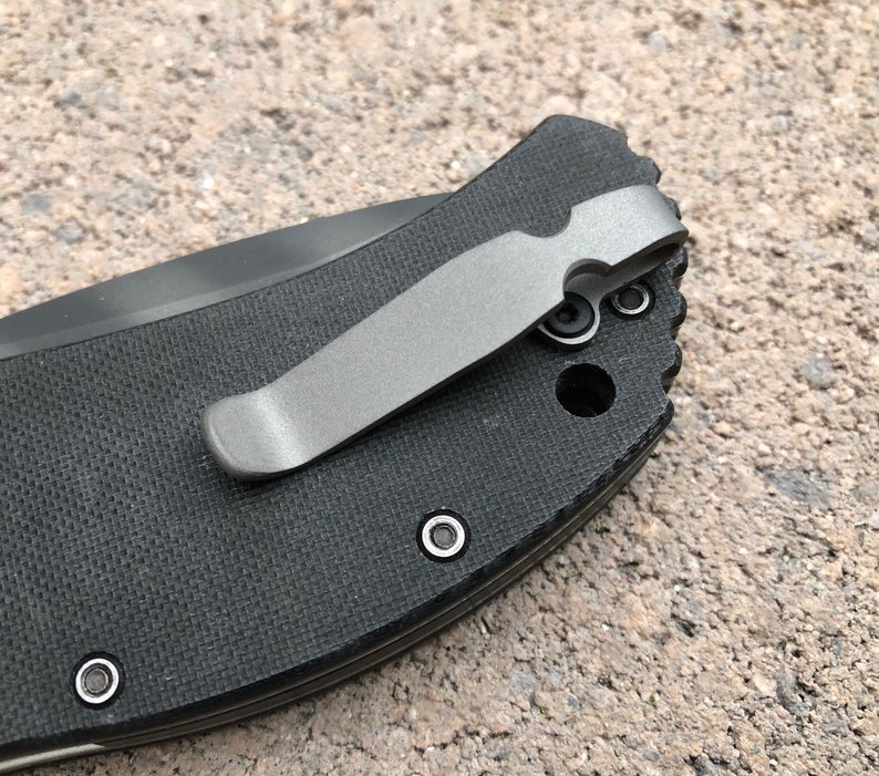 May include: A black pocket knife with a silver pocket clip. The knife has a textured black handle and a silver pocket clip.