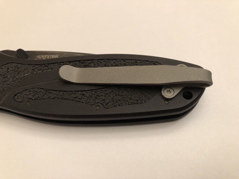 May include: Black pocket knife with a textured handle and a silver pocket clip. The knife has a small screw on the side and the text "1670TSTBW" is engraved on the handle.