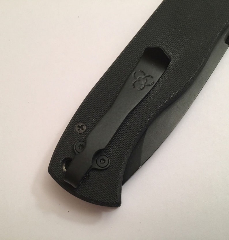 May include: Black pocket knife with a black pocket clip. The pocket clip has a logo on it.