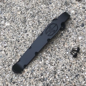 May include: A black metal key chain with a Spartan helmet logo. The keychain has a loop for attaching keys and two screws.