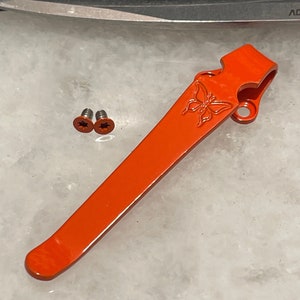May include: Orange metal pocket clip with a butterfly design. Two small silver screws are included.