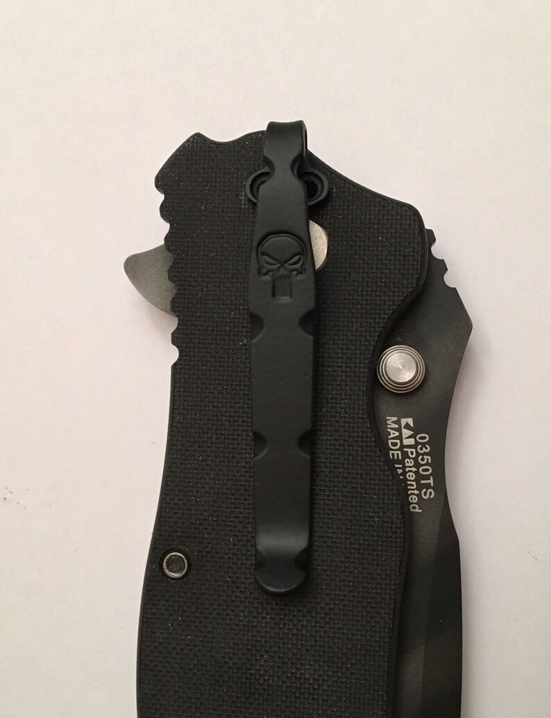 Pu&ograve; includere: Coltellino tascabile nero con un clip a forma di teschio e il testo "0350TS MADE Patented" sul lato.