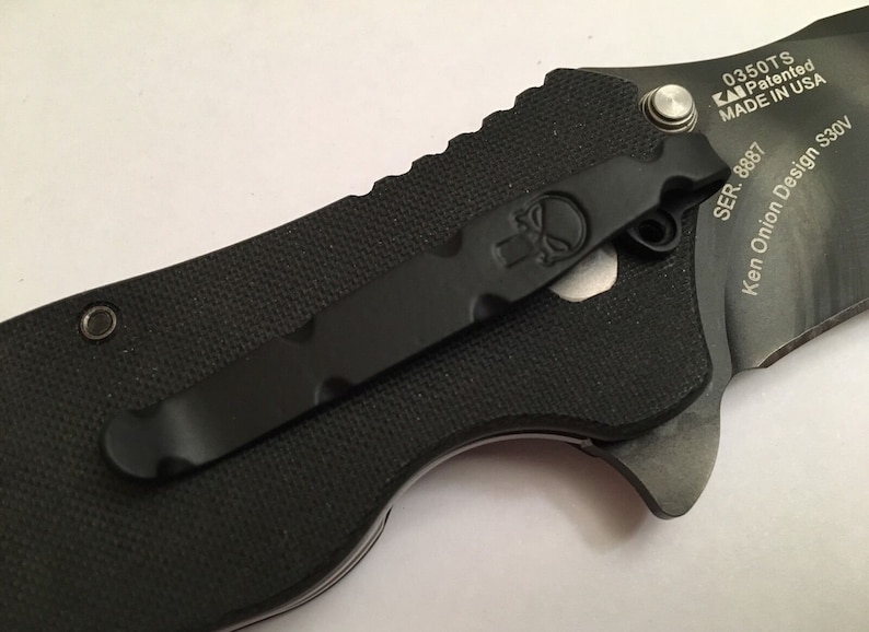 Pu&ograve; includere: Coltellino da tasca nero con clip nero e logo a forma di teschio. Il coltellino ha inciso sul lato il testo "0350TS KAI Patented MADE IN USA SER. 8887 Ken Onion Design S30V".