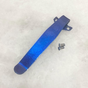 May include: A metallic blue pocket clip with a gradient effect, accompanied by two small screws. The clip has a curved end and two holes for attachment. The overall design is sleek and modern.