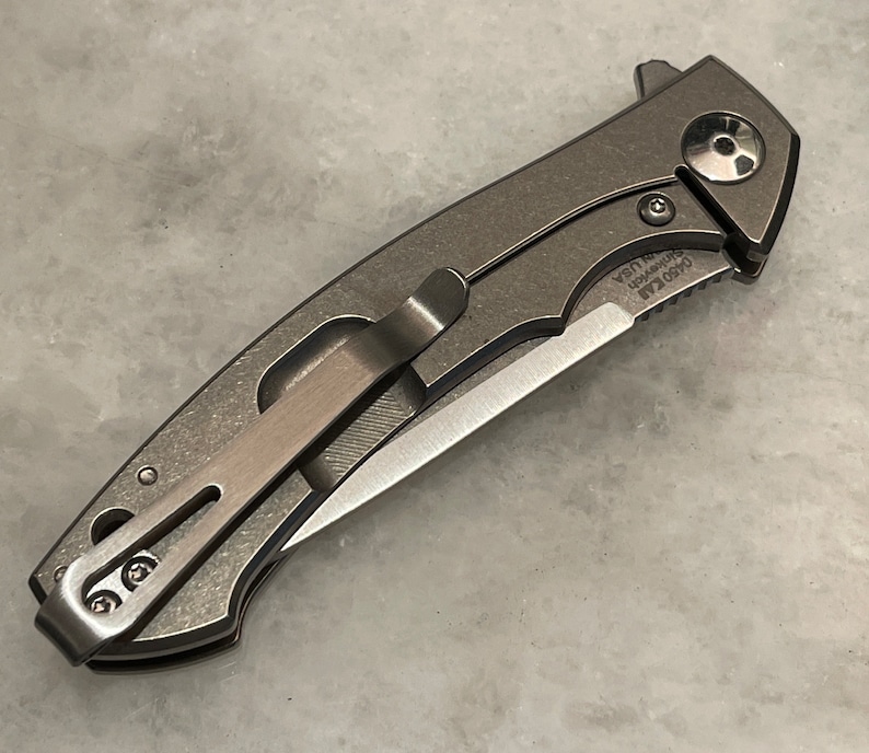 May include: A gray pocket knife with a partially serrated blade and a pocket clip. The knife has a black skull design on the handle and the text "0450 Kai USA" is engraved on the handle.