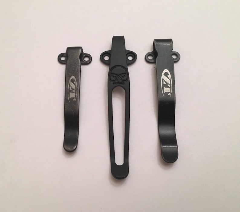 Puede incluir: Tres clips de bolsillo de metal negro con un logotipo ZT. El clip del medio tiene un dise&ntilde;o de calavera.