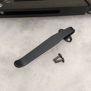 May include: Black metal pocket clip with two silver screws. The clip is designed to attach to a pocket knife or other tool.