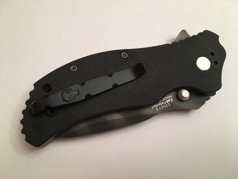 Pu&ograve; includere: Coltello pieghevole nero con un fermaglio da tasca nero e una vite del fermaglio da tasca argentata. Il coltello ha un'impugnatura nera e una lama argentata. La lama &egrave; parzialmente aperta. Il coltello ha il testo "03501S KAI brevettato MADE in" sul lato.