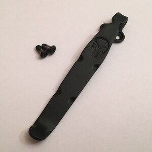 Pu&ograve; includere: Clip da tasca in metallo nero con un design a forma di teschio e due viti.