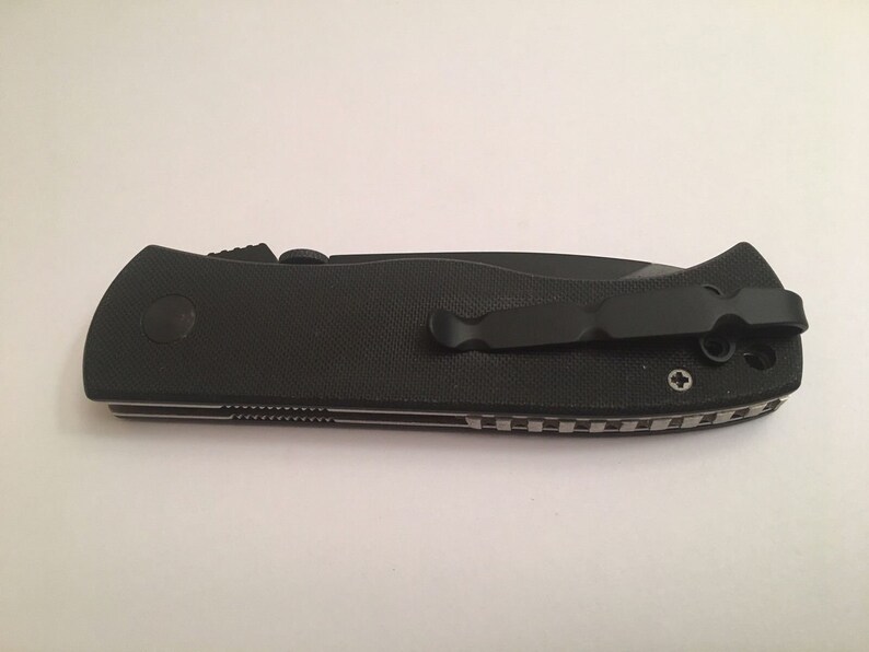 May include: Black folding knife with a textured handle and a black pocket clip. The knife has a silver screw on the handle.