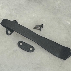 May include: Black metal pen clip with two screws. The clip is curved and has a smooth, matte finish.