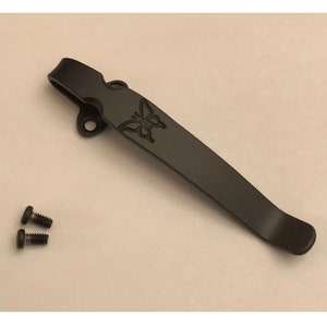 May include: A black metal pocket clip with a butterfly design. The clip is designed to attach to a pocket knife or other tool. Two small black screws are included.