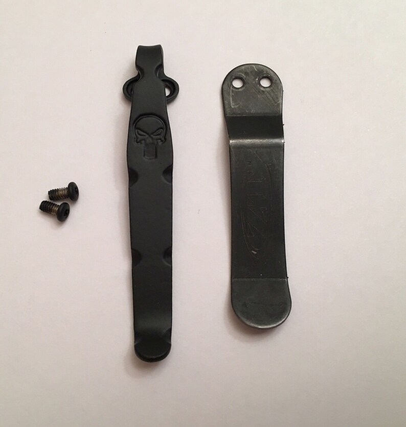 Pu&ograve; includere: Due clip da tasca in metallo nero, una con un design a forma di teschio e l'altra con un logo. Sono inclusi due piccoli viti nere.